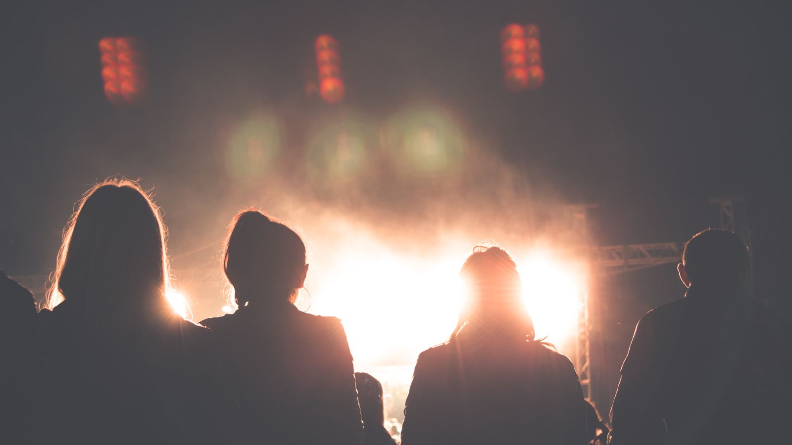 Fans seen from behind, silhouetted against warm stage lights
