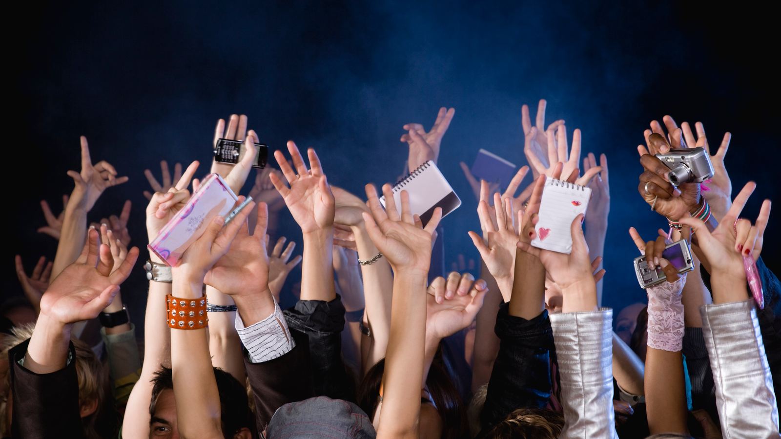 Fans reaching up with raised hands, notebooks and cameras at an event