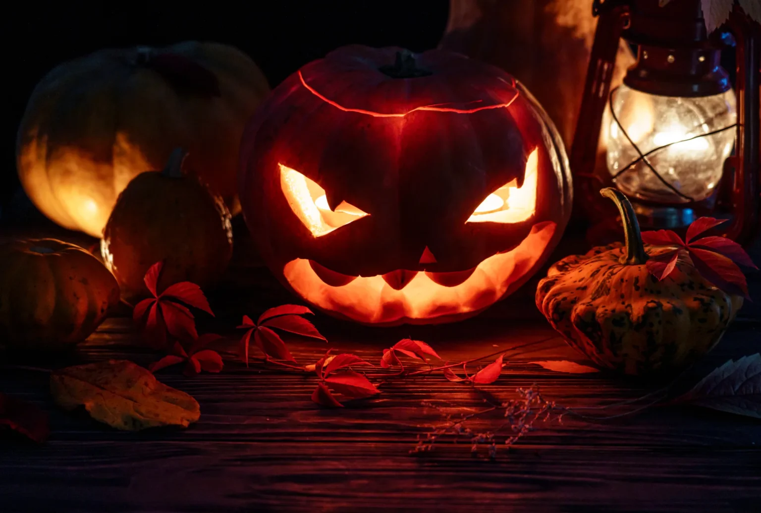 Carved jack-o-lanterns glowing in the dark beside an old lantern