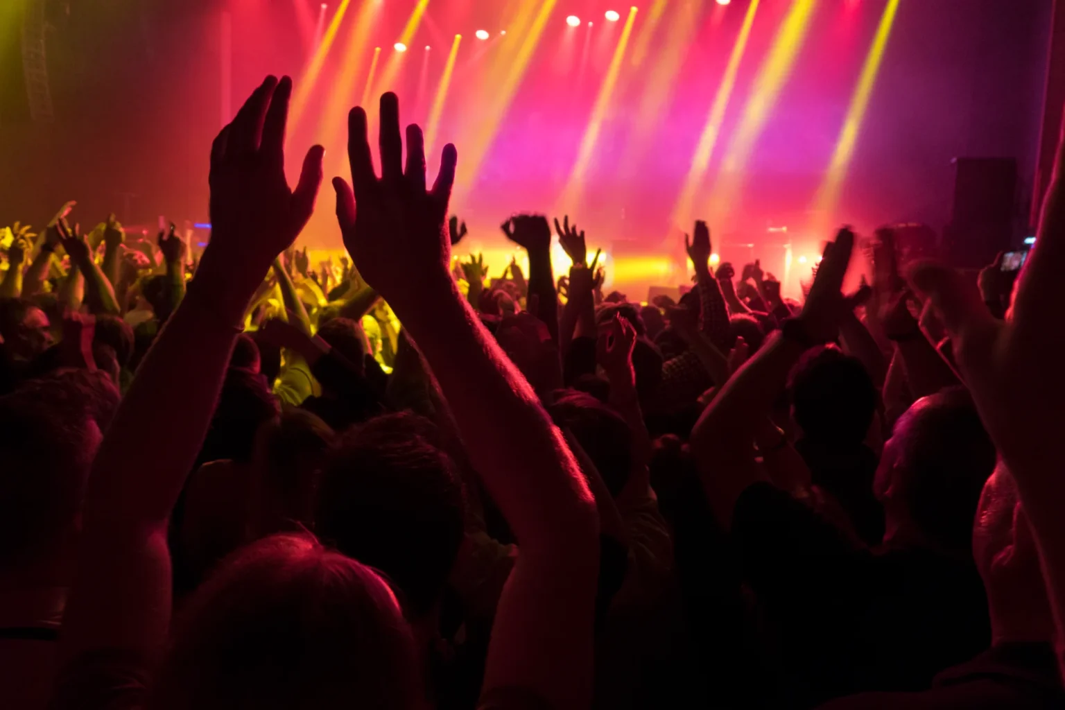 Concert crowd with hands raised in front of a stage lit in red and yellow