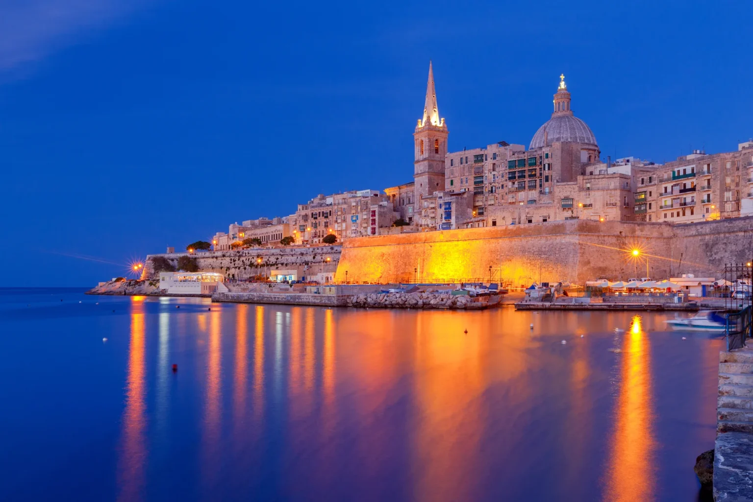 Valletta skyline lit up at night, reflected in Marsamxett Harbour