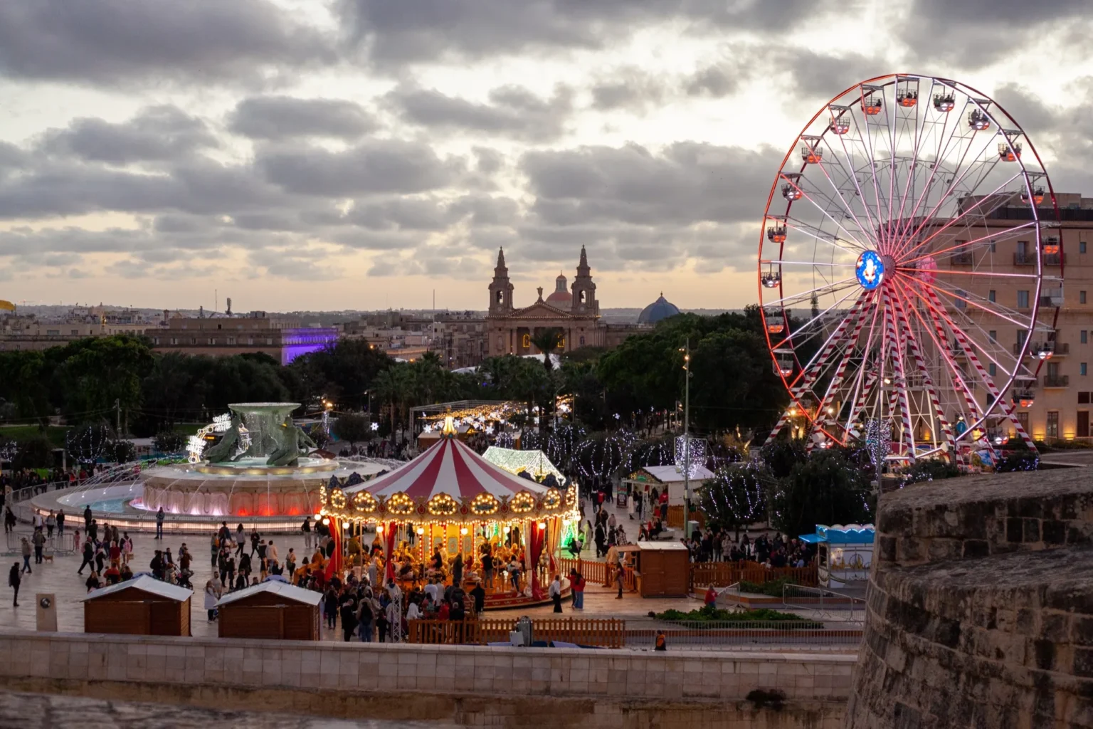 Christmas village with a carousel and ferris wheel by the Triton Fountain outside City Gate, Valletta